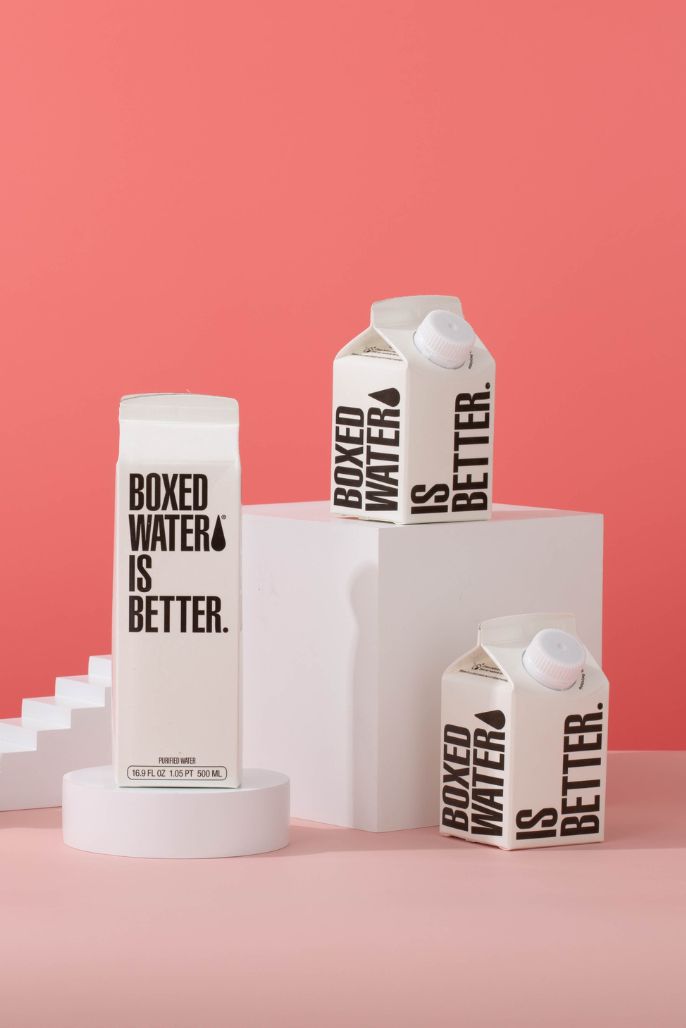 a 250 ML and 500 ML Boxed Water box on a pedestal in front of a pink background