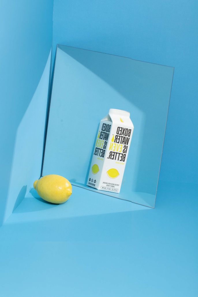 A lemon and Lemon Boxed Water in front of a mirror