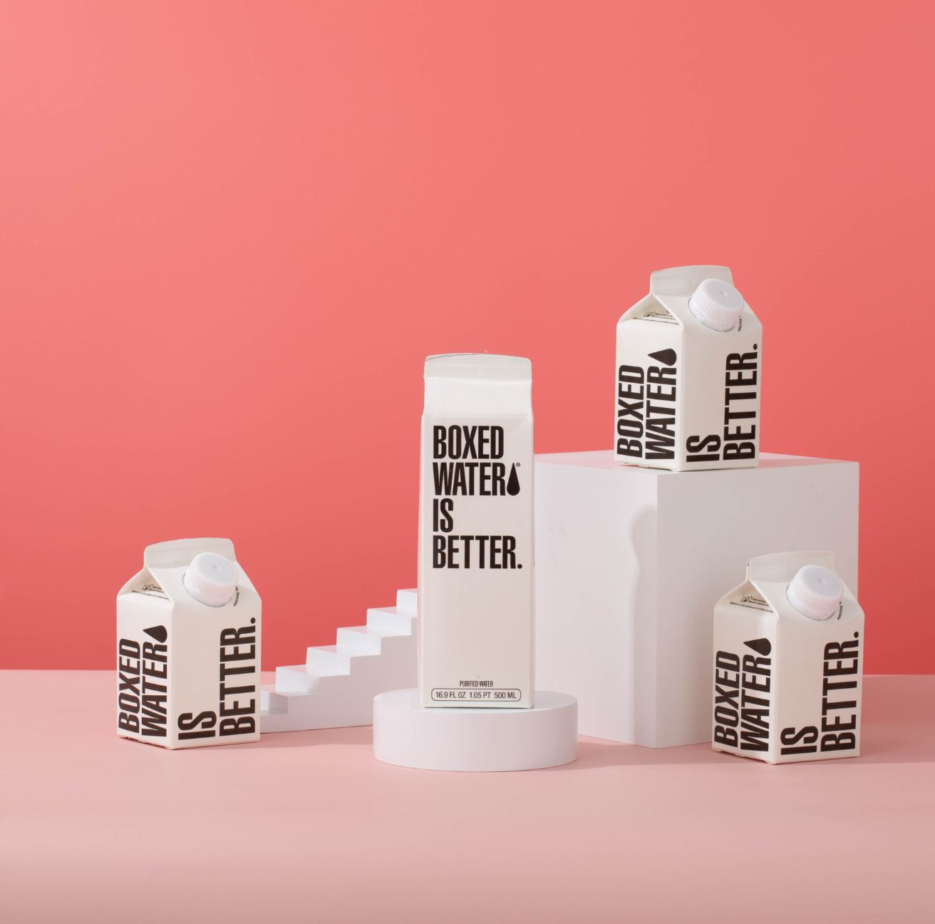 a 250 ML and 500 ML Boxed Water box on a pedestal in front of a pink background