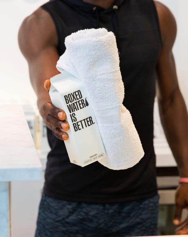 Man in fitness apparel handing Boxed Water carton and white towel