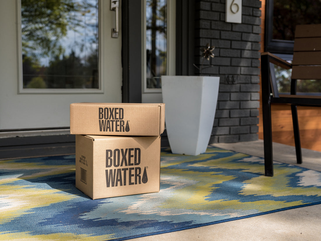 Two corrugate boxes of Boxed Water at a doorstep on a striped rug