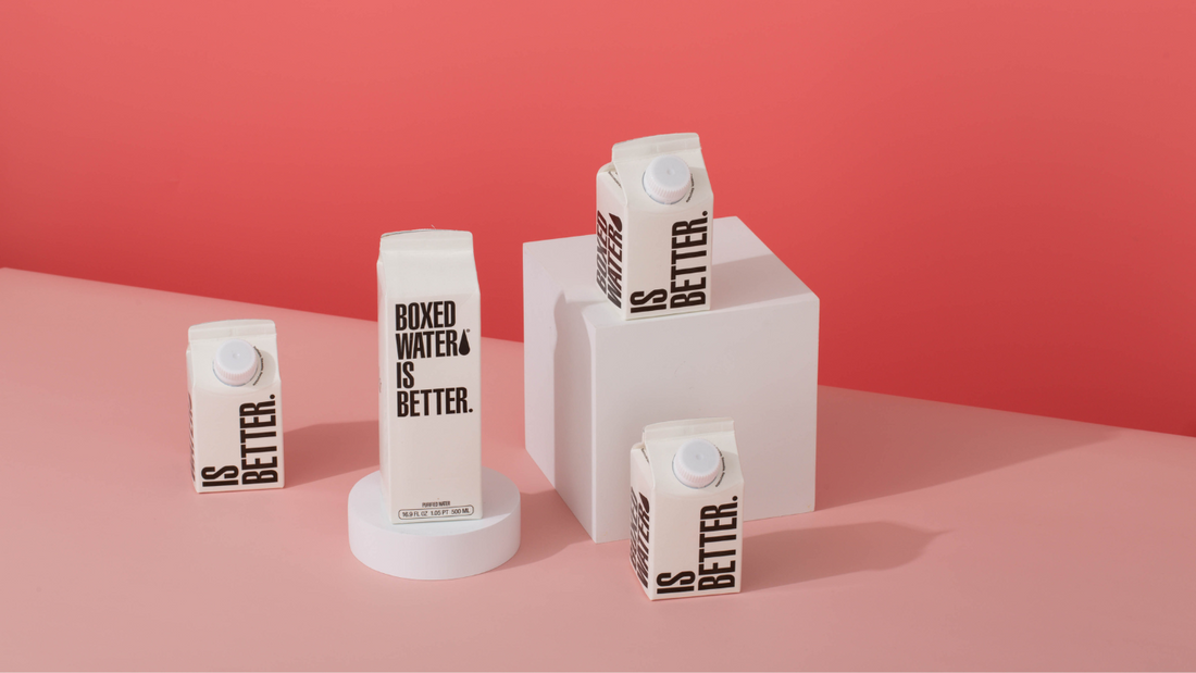 Four boxes of Boxed Water on pedestals with pink backdrop 