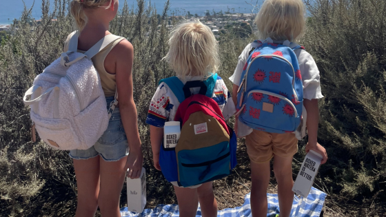 Three young kids holding Boxed Water and wearing bakcpacks
