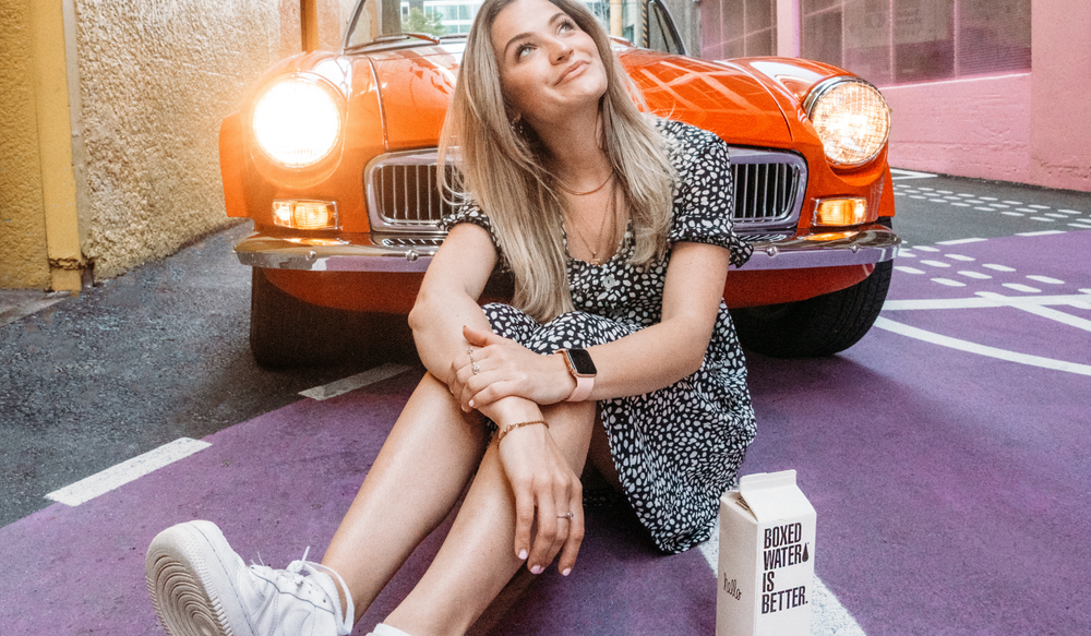 Young woman sitting with Boxed Water in front of a red car