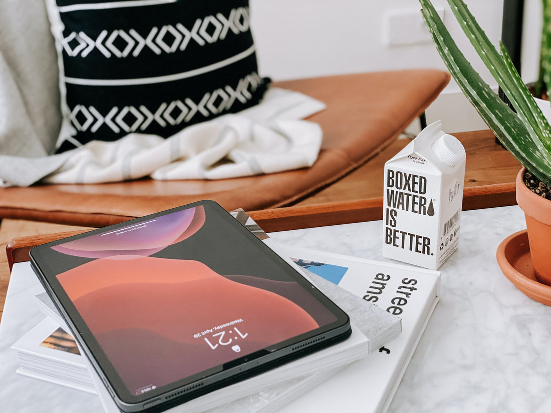 An I pad, book, Boxed Water, and plant on a coffee table