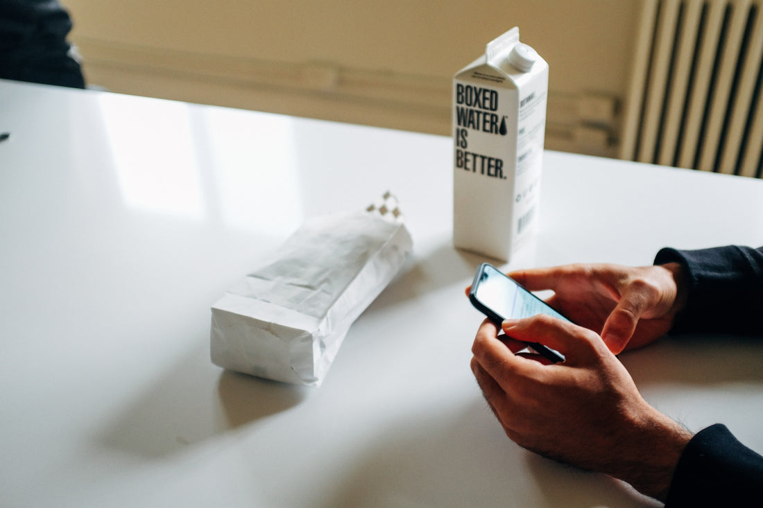 Person looking at phone at a white table with a Boxed Water