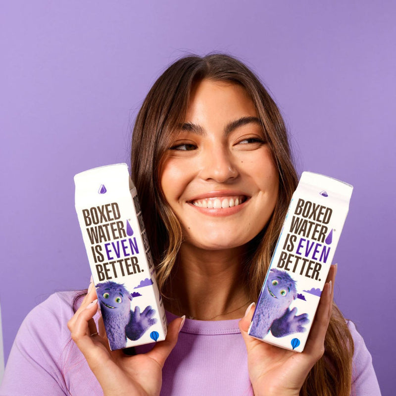 female in purple background holding two IF boxes of boxed water