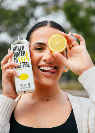 Woman with Lemon Boxed Water holding lemon slice and sticking out tongue
