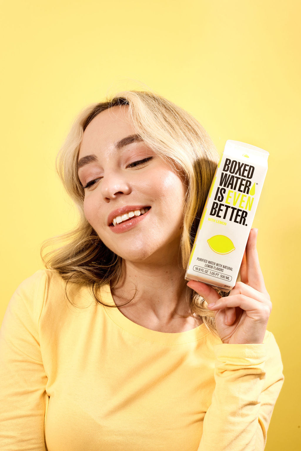 Yellow background with woman holding lemon flavored boxed water