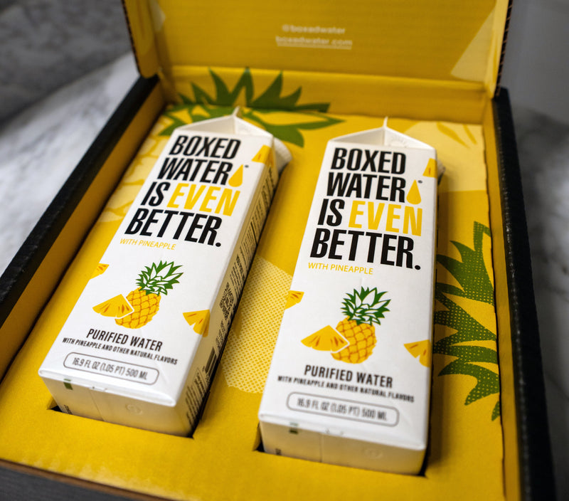 Two boxes of Pineapple Boxed Water on a yellow background with branding text.