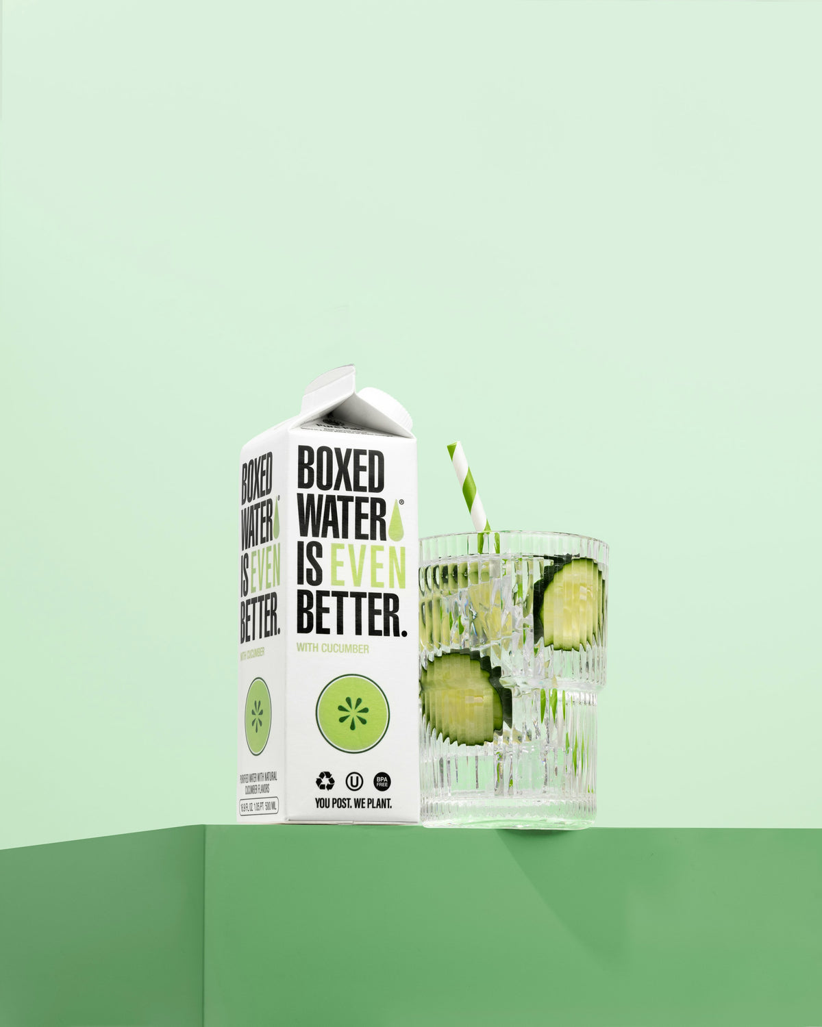 Cucumber flavored Boxed Water next to glass with cucumber slices and paper straw