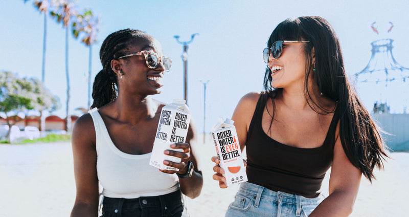 Two woman smiling at each other and drinking Boxed Water