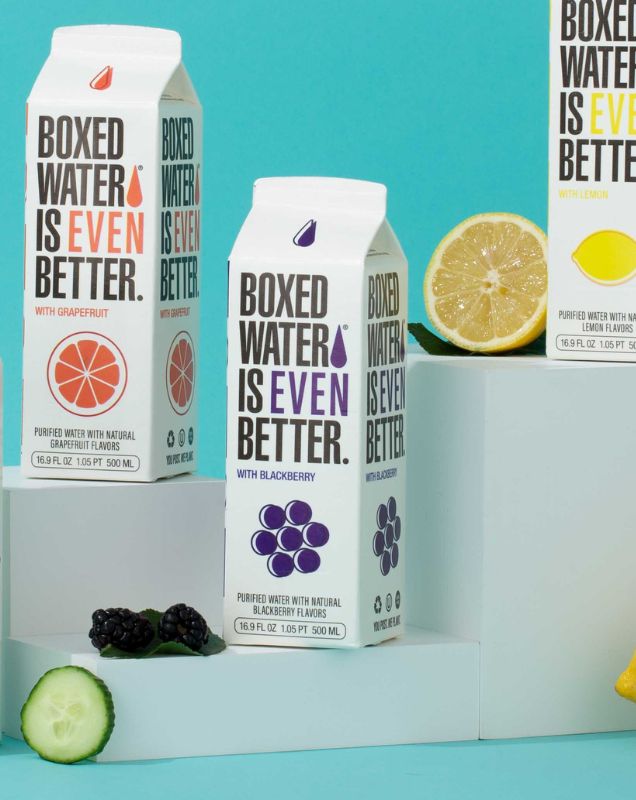 Fruit flavored boxed water on pedestal with teal background and fresh fruit displayed