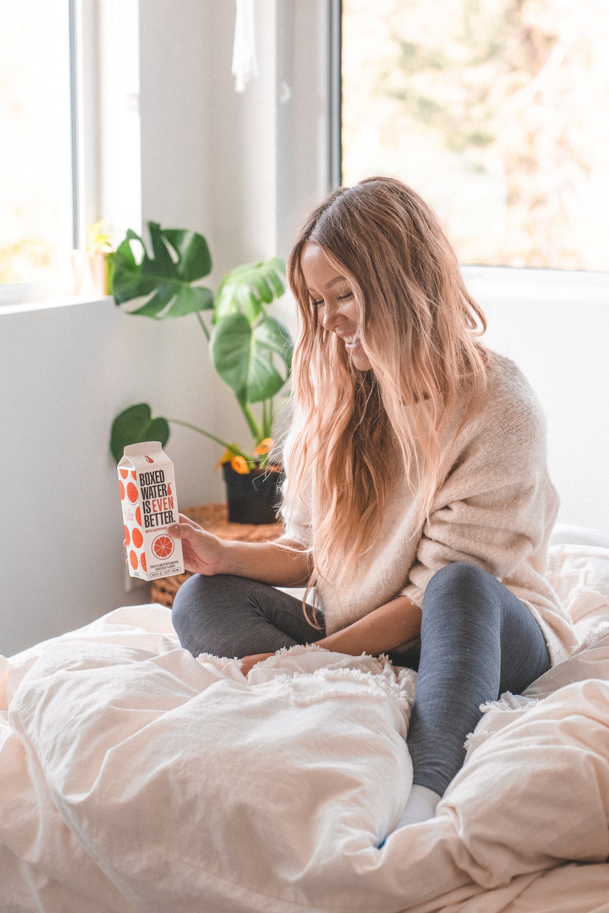 Woman in messy bed smiling with Grapefruit Boxed Water