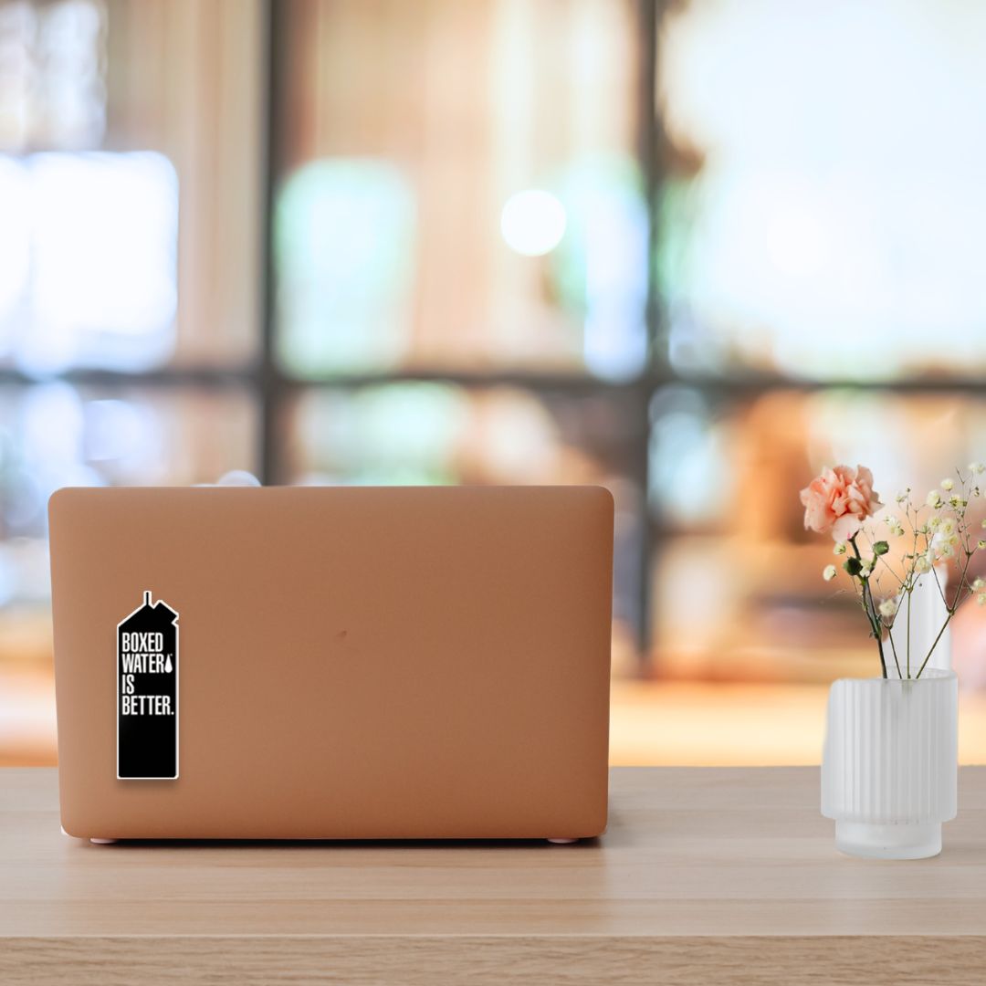 Black Boxed Water Sticker on a laptop on an office desk next to flowers