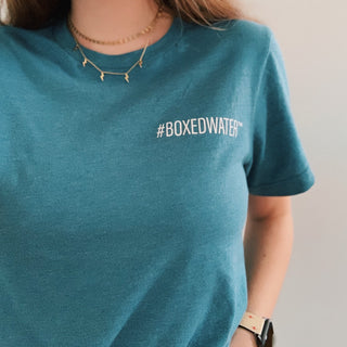 Female wearing teal Boxed Water t-shirt that says #BOXEDWATER