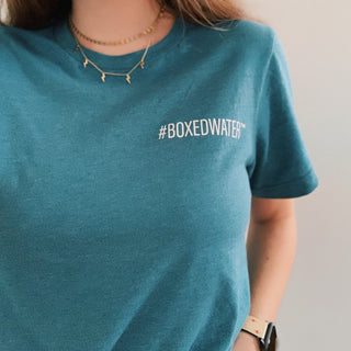 Female wearing teal Boxed Water t-shirt that says #BOXEDWATER 