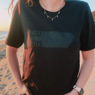 Female model wearing Boxed Water t-shirt that says Reach for Better on the beach